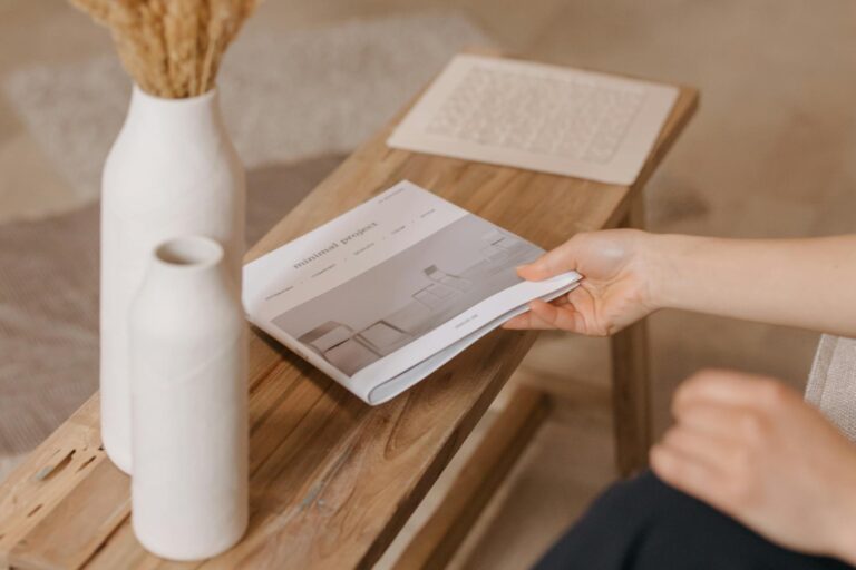 A person reads a magazine on a wooden bench beside ceramic vases, showcasing minimalist decor.